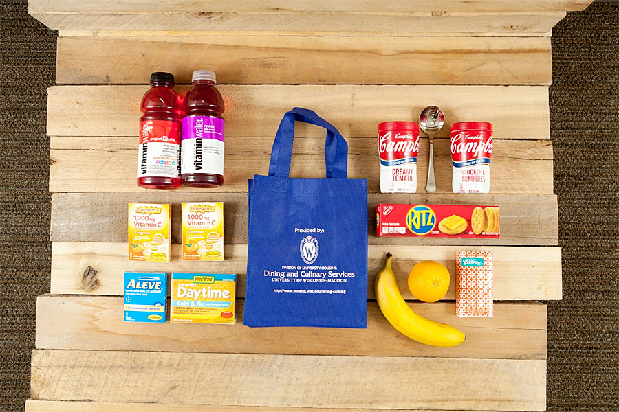 Assorted food, snacks, medicine and toiletries positioned around a blue reusable Dining and Culinary Service bag. 