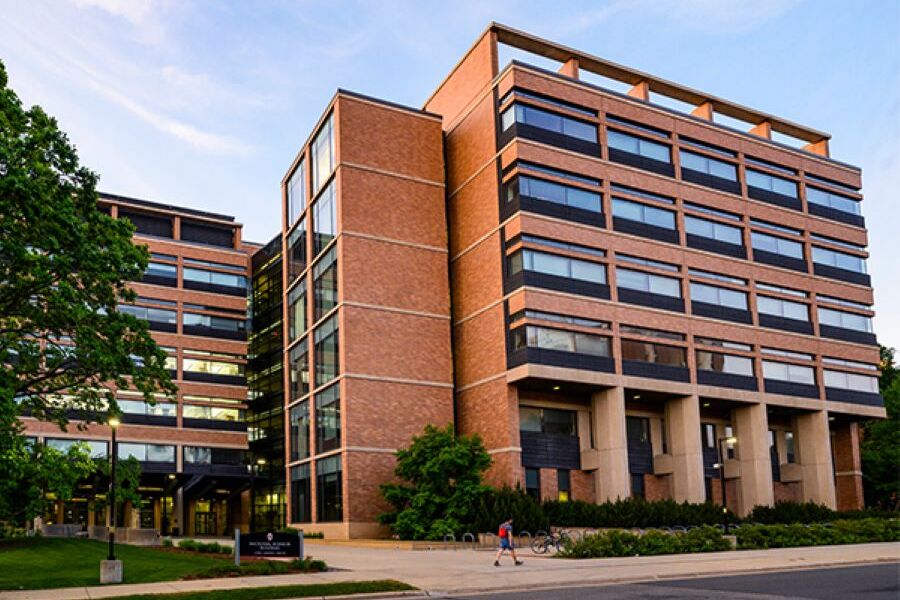 Microbial Sciences Building exterior with individual walking on sidewalk. 