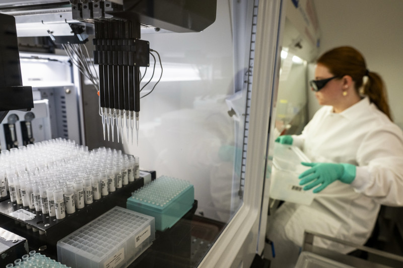A Biomek i5 liquid handling machine processes samples of milk, with a researcher in medical protective equipment nearby.